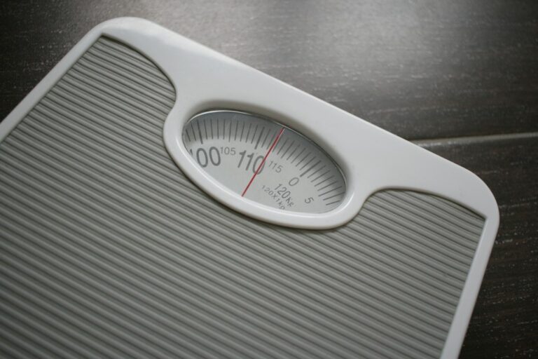 An analog bathroom scale with a dial on a tiled floor