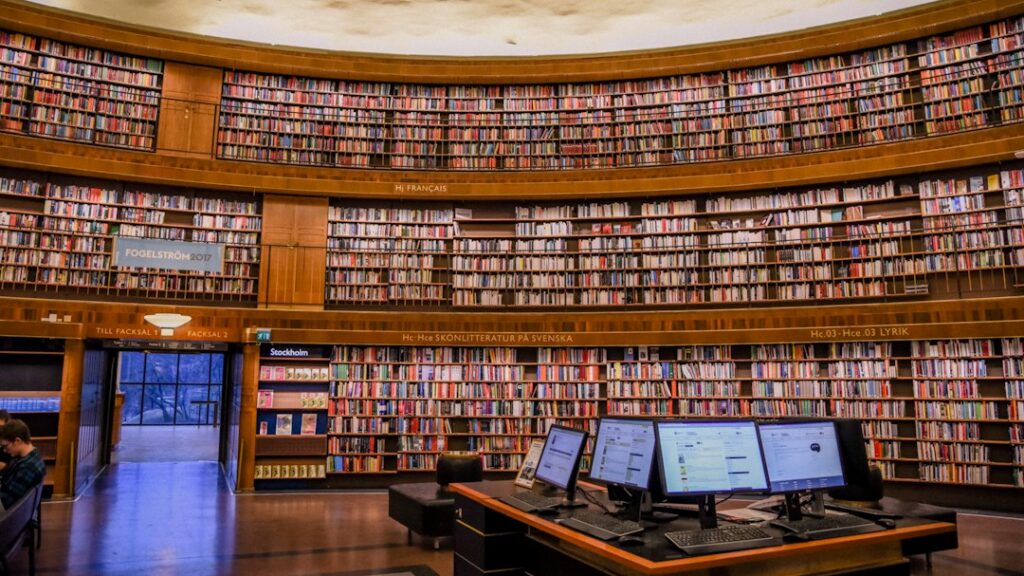 Computer terminals in front of curved bookshelves in a library.