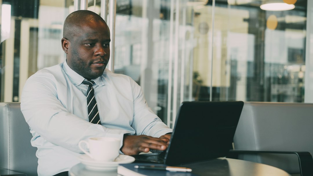 Man in a shirt and tie using a laptop at a cafe table.