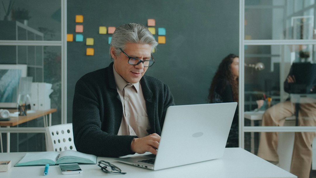 Man with glasses smiling while working on a laptop.