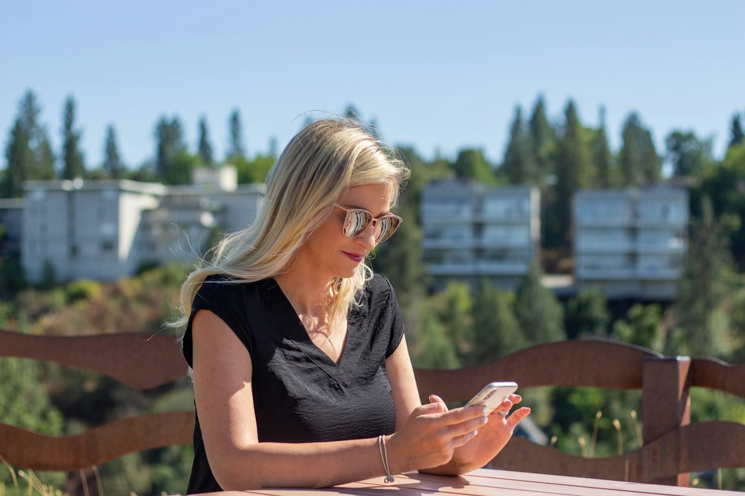 Woman with glasses using a phone at an outdoor table.