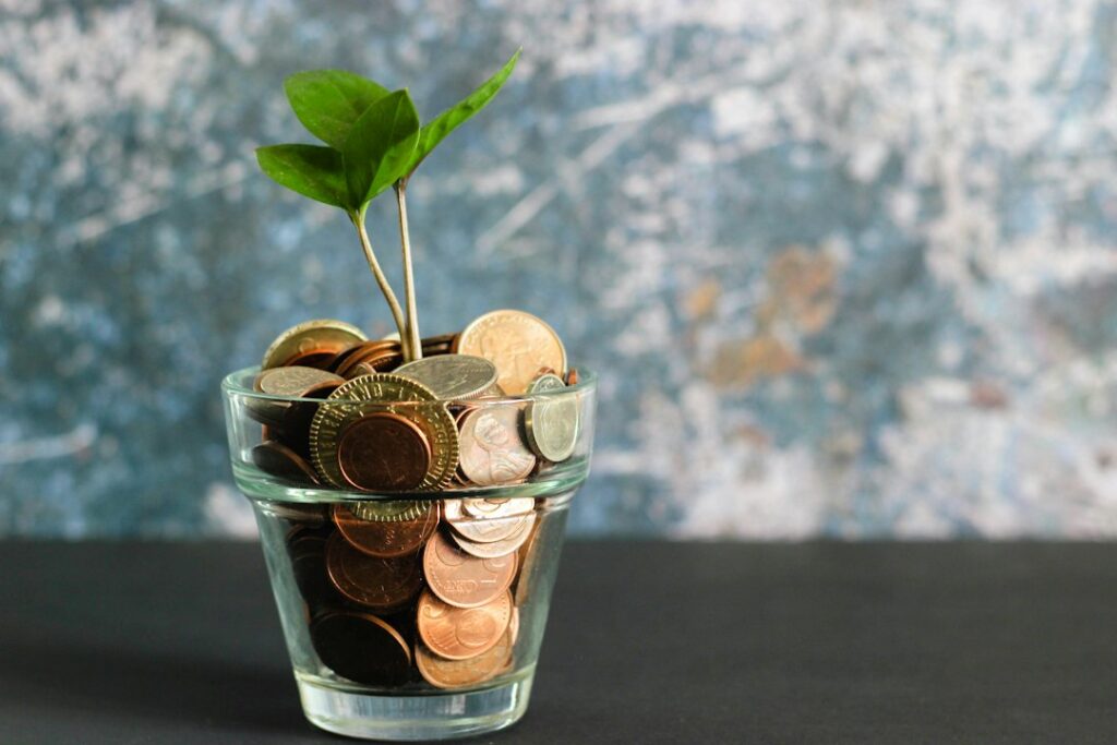 A small green plant growing from a glass filled with coins.