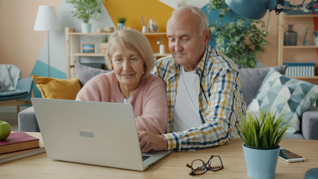 Older adults using a laptop together in a bright home.