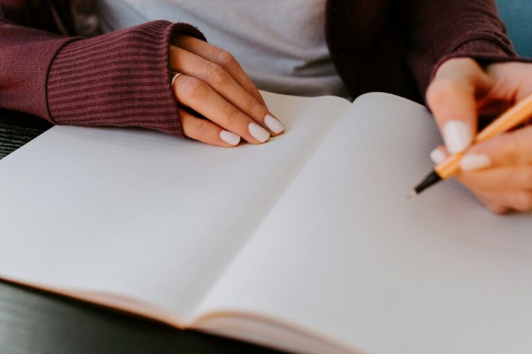 Hands holding a pencil over an open blank notebook.