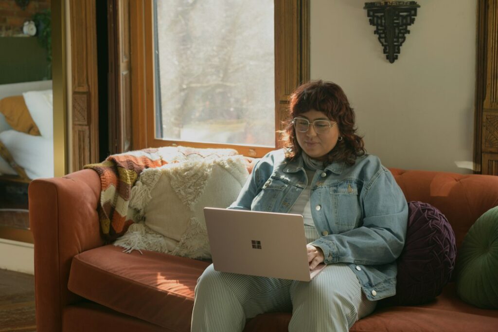 A woman using a laptop while sitting on a sofa at home